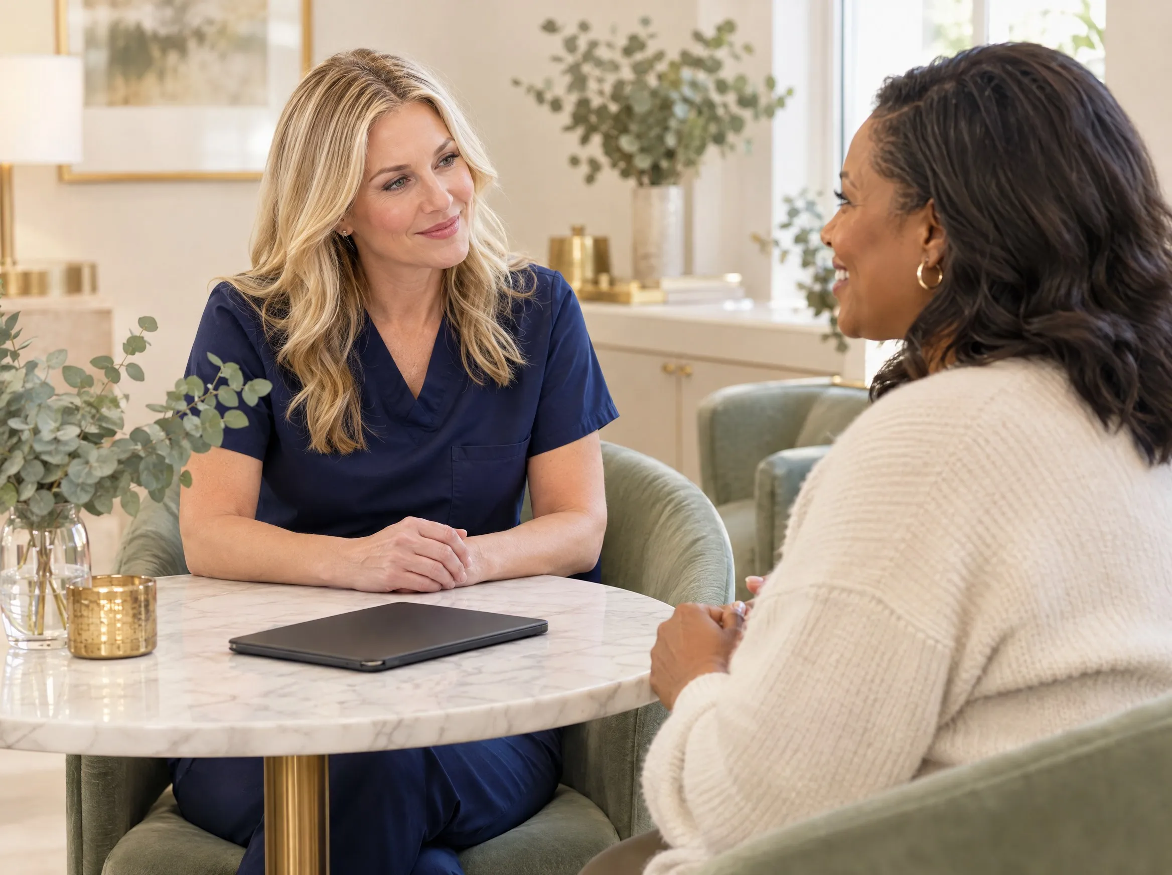 A med spa provider in navy scrubs listening to a client during a relaxed consultation